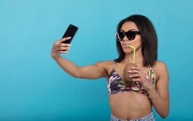 夏の自撮り 携帯電話で新鮮なカクテルで自分を撮影する水着の黒人の女の子 プレミアム写真