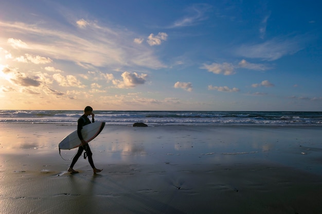 Premium Photo | Surfer Walking On The Beach At Sunset.