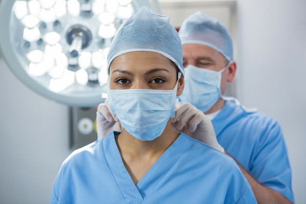 Premium Photo | Surgeon helping in tying surgical mask to his co-worker