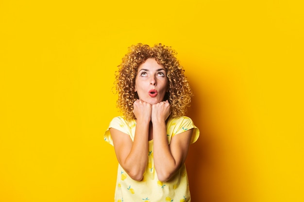 Premium Photo Surprised Curly Haired Young Woman Looks Up Holding Fists Under The Chin On A 