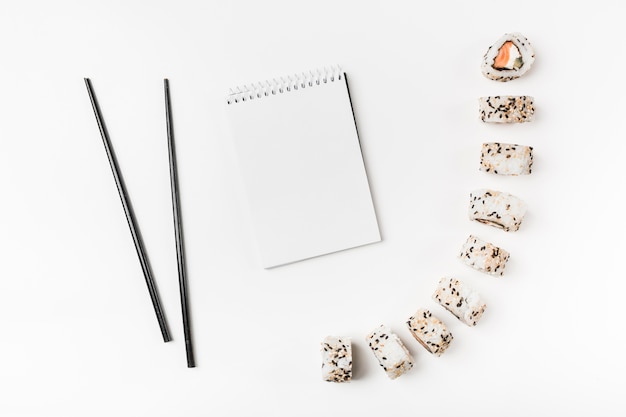 Sushi rolls with chopsticks and spiral notepad on white background Free Photo