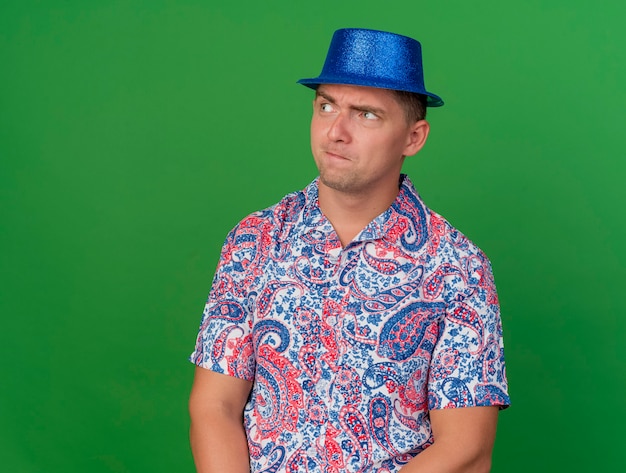 Free Photo | Suspicious young party guy wearing blue hat isolated on green