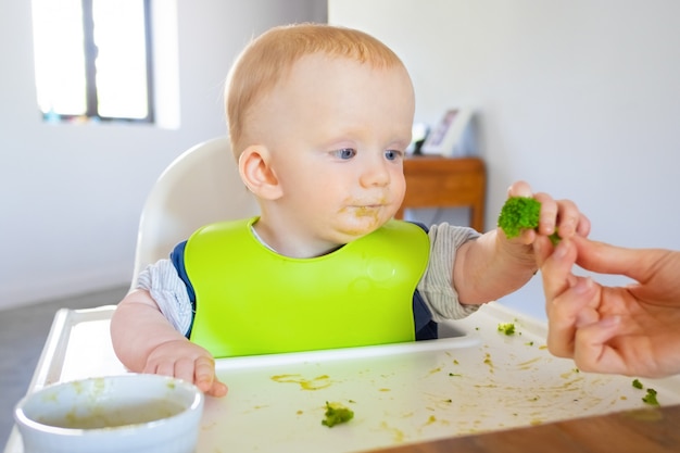 Free Photo | Sweet baby in bib taking broccoli piece from mom