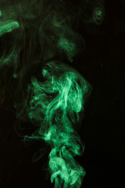 黒の暗い背景に対して緑の煙の渦 無料の写真