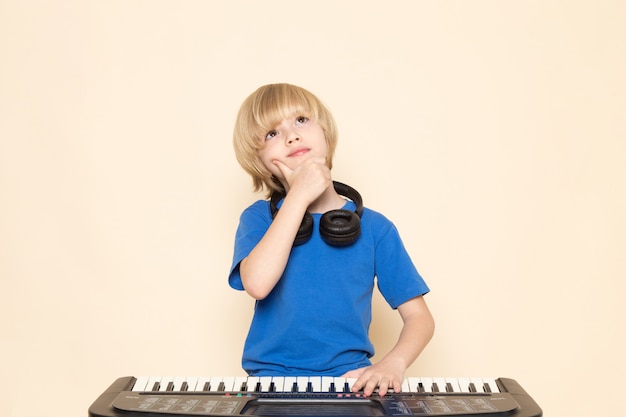 小さなかわいいピアノ思考ポーズを演奏する黒いヘッドフォンと青いtシャツの正面かわいい男の子 無料の写真