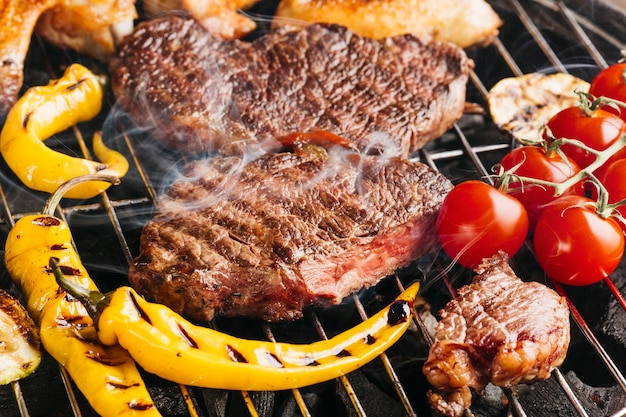 Tasty beef steaks on the grill with yellow chili and cherry tomato Free Photo