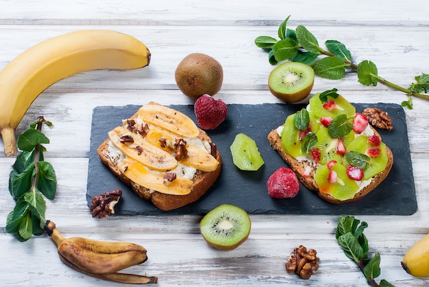 Tasty sweet sandwiches with bananas, nuts and chocolate, kiwi, strawberries and mint on wooden table Premium Photo