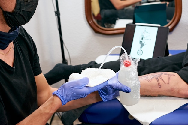 Premium Photo The Tattoo Artist In Blue Gloves Cleaning The Newly Completed Tattoo On A Man S Leg