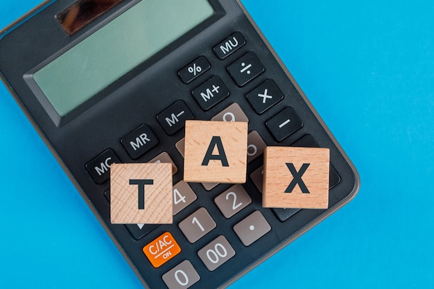 Tax planning concept with wooden cubes on calculator on blue table flat lay. Free Photo