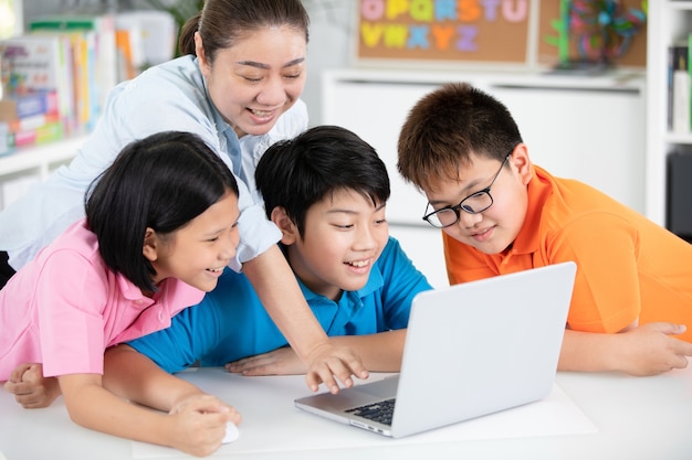 Teacher and cute asian children using laptop computer together ...