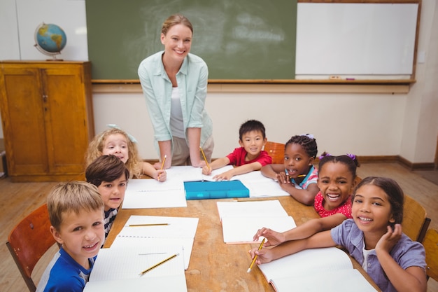 Teacher And Pupils Working At Desk Together At The Elementary