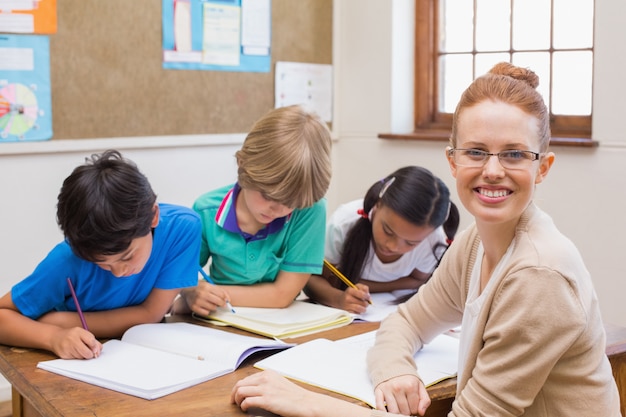 Teacher And Pupils Working At Desk Together At The Elementary