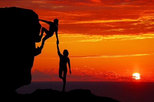  Teamwork couple hiking help each other trust assistance silhouette in mountains, sunset. teamwork o