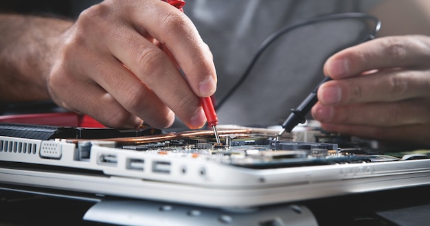 Technician hands checking motherboard with multimeter. Premium Photo