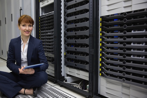 Technician sitting on floor beside server tower using tablet pc Premium Photo
