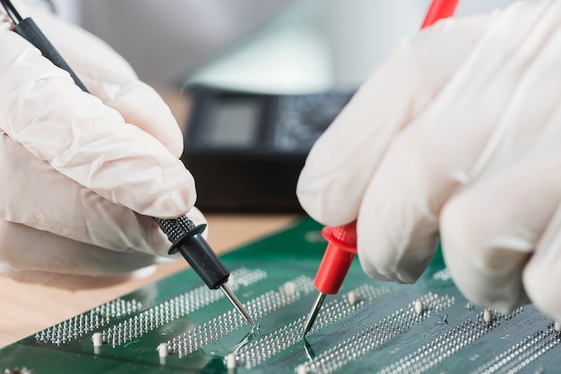 Technician wearing gloves examining computer circuit board with digital multimeter Free Photo