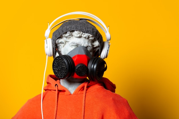 オレンジ色のパーカー フェイスマスク 黄色の背景にヘッドフォンで帽子の十代の彫刻 プレミアム写真
