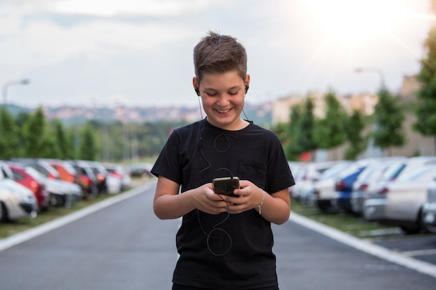 Teenage boy smiling while texting his friends via social networks using mobile phone, sitting against urban landscape Premium Photo