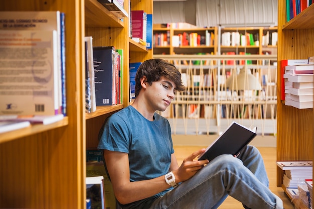 Free Photo | Teenager reading on floor between bookshelves