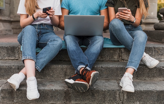 Teens sitting on stairs and working on phones and laptop Free Photo