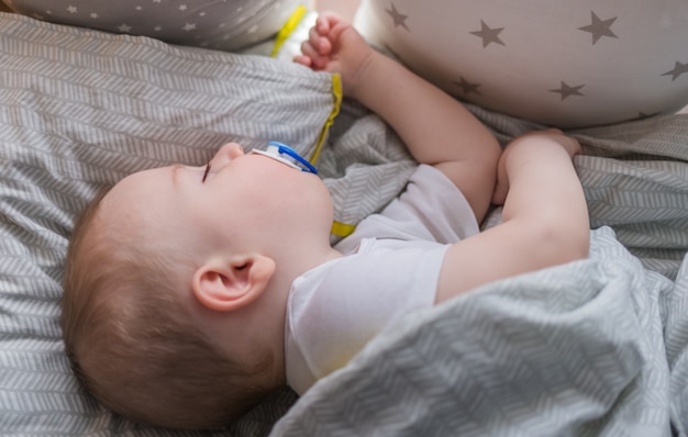 赤ちゃんはベビーベッドで寝ています おしゃぶりを持った少年の白日夢 ベビーベッドで寝る プレミアム写真