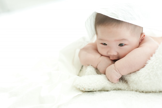 赤ちゃんは白い背景の白いベッドの上で正面を見つめています プレミアム写真