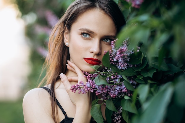 The charming girl stands near bushes with flowers Free Photo