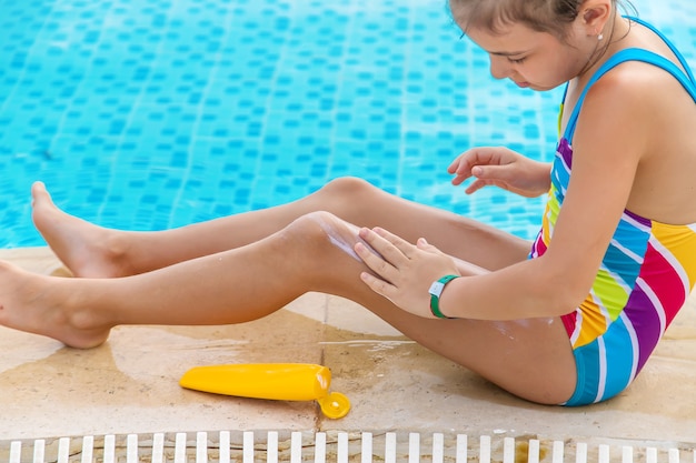 子供はプールのそばの彼女の足に日焼け止めを置きます プレミアム写真