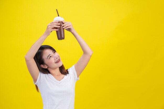 女の子は黄色の透明なプラスチックガラスからココアの冷たい水を飲みます 無料の写真