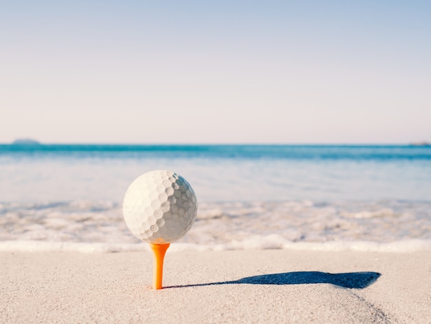ゴルフボールはティーの上にあり 海を背景に砂浜に刺されています プレミアム写真