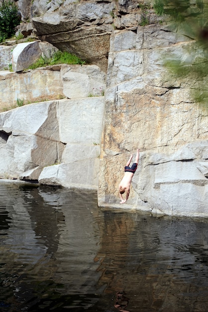 男は峡谷で水中の岩からジャンプします 大胆不敵な人 高い高さと深い湖 プレミアム写真