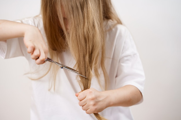 子供の女の子は白い背景のはさみで彼女の長い髪を刈り取ります 赤ちゃんのためのファッショナブルなヘアカット 美容師 子供のいたずら 散髪 プレミアム写真