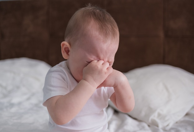 子供は動揺しています 赤ちゃんはベッドに座って泣く プレミアム写真
