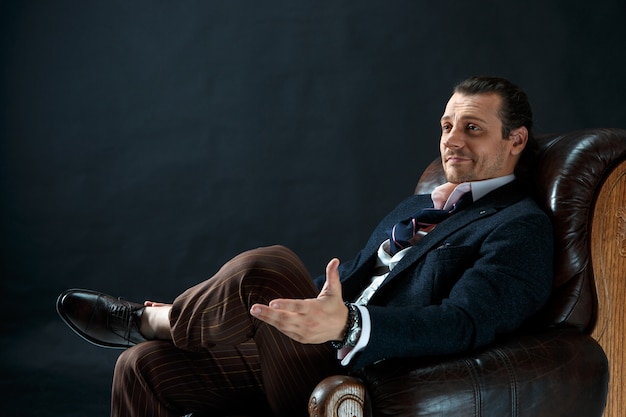 灰色のスタジオでスーツを着た成熟したスタイリッシュな男。肘掛け椅子に座っている実業家 無料写真