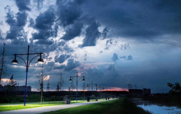 雨雲の空を背景に提灯が灯る川の近くの都市公園の小道 プレミアム写真