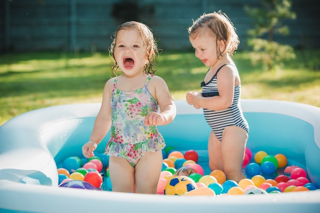 夏の晴れた日に膨脹可能なプールでおもちゃで遊ぶ2人の小さな女の赤ちゃん 無料の写真