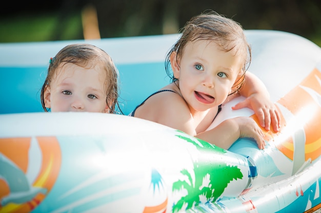 無料の写真 夏の晴れた日に膨脹可能なプールでおもちゃで遊ぶ2人の小さな女の赤ちゃん