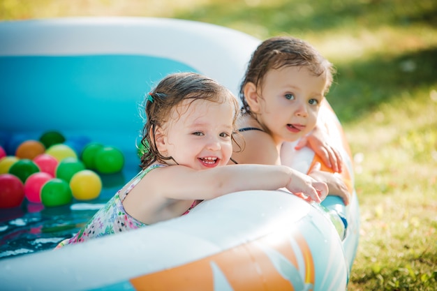 夏の晴れた日に膨脹可能なプールでおもちゃで遊ぶ2人の小さな女の赤ちゃん 無料の写真