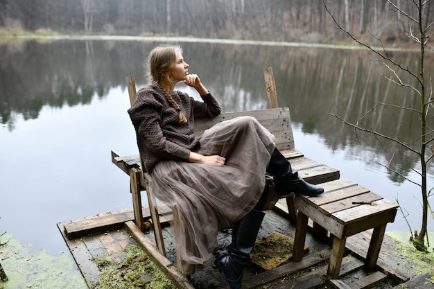 女性は湖のほとりに座っています 孤独な女性 湖のある秋の森 プレミアム写真