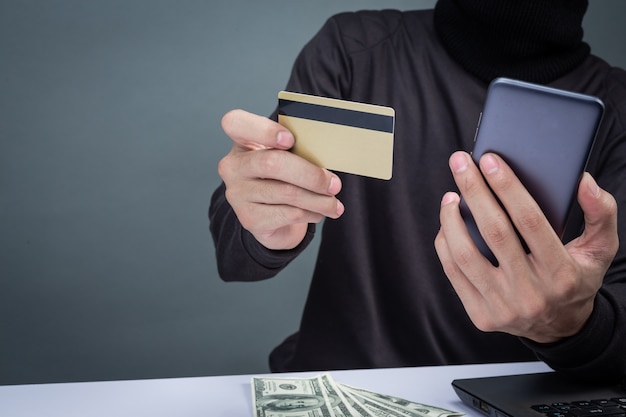 Thieves wear a black hat, hold the phone and a smart card on gray Free Photo