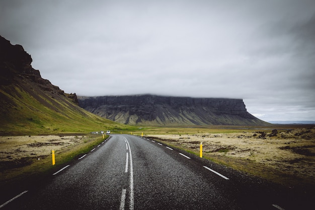 Free Photo | A thin road in a green field with hills and grey cloudy ...