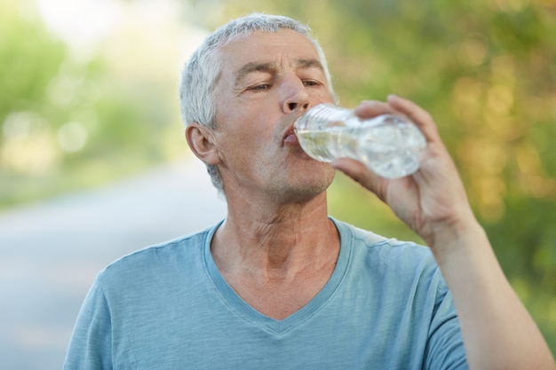 喉が渇いたシニア男性がペットボトルから水を飲む プレミアム写真