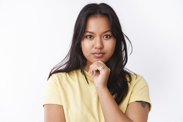 Free Photo Thoughtful Attractive Young Malaysian Girl With Facial Scars And Acne Touching Chin And Looking Determined At Camera Thinking Standing Dreamy Against White Background In Yellow T Shirt