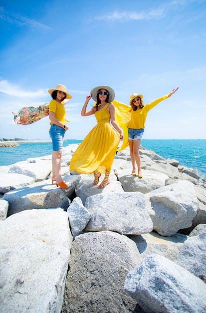 正午の太陽の光に対して海のビーチに立っている黄色の服を着ている3つのアジアの女性 プレミアム写真 正午の太陽の光に対して海のビーチに立っている黄色の服を着ている3つのアジアの女性 プレミアム写真