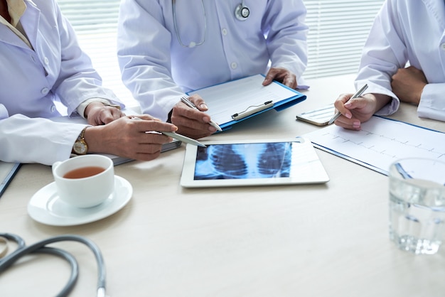 Three cropped doctors analyzing chest x-ray on the digital pad Free Photo