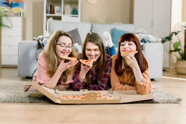 Premium Photo Three Female Friends Eating Pizza At The House Party While Lying On The Floor In Cozy Room