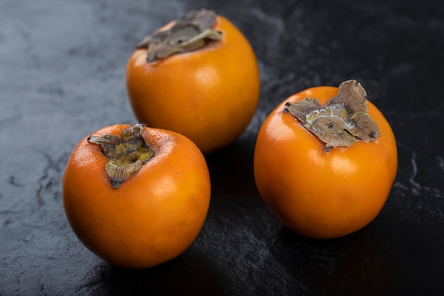 Premium Photo | Three fresh fuyu persimmons placed on black surface.