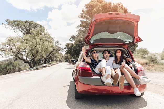 3人の友人が車の幹の中に一緒に座って道路に自画像を撮る プレミアム写真