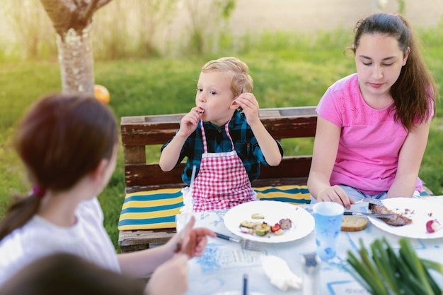 Premium Photo | Three kids sitting by the table in nature and eating.