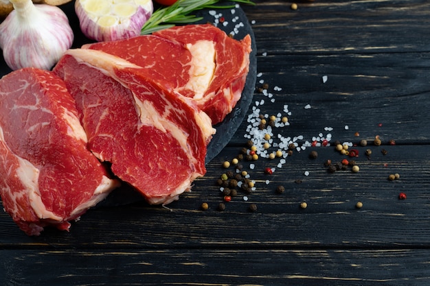 Three pieces of juicy raw beef with vegetables on a stone cutting board Premium Photo